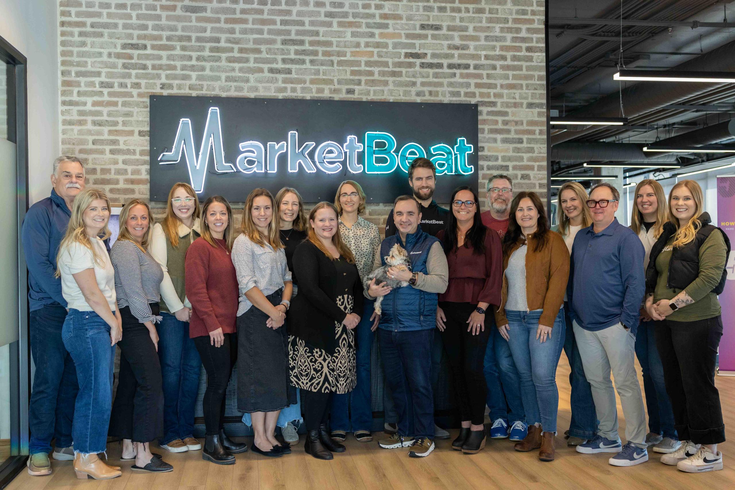 MarketBeat Staff in front of neon MarketBeat sign